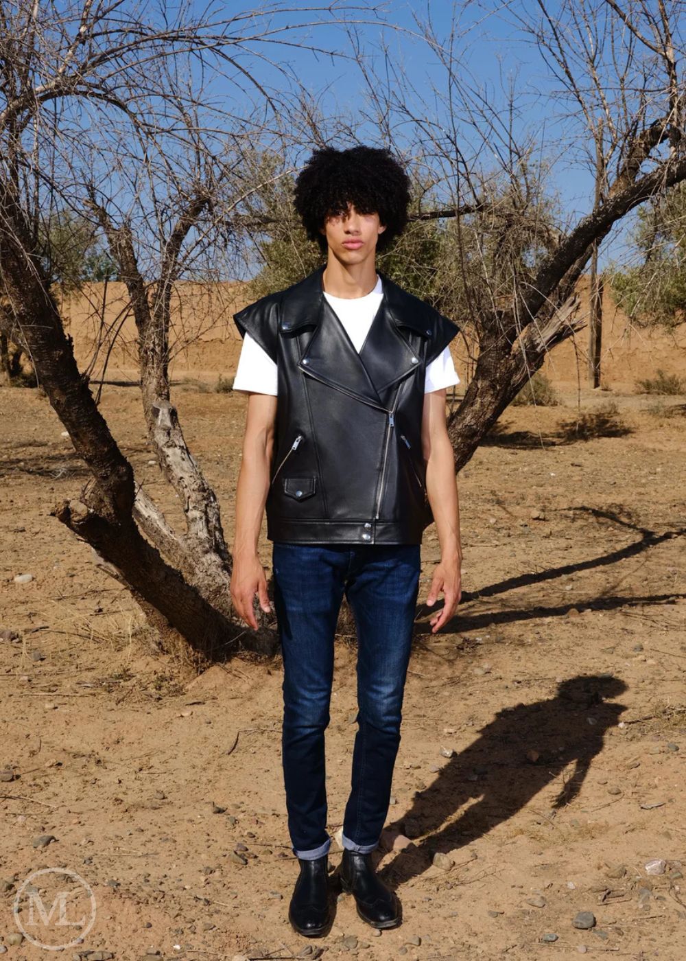 Men wearing a black leather vest, white shirt, blue jeans, and black shoes in a desert setting.
