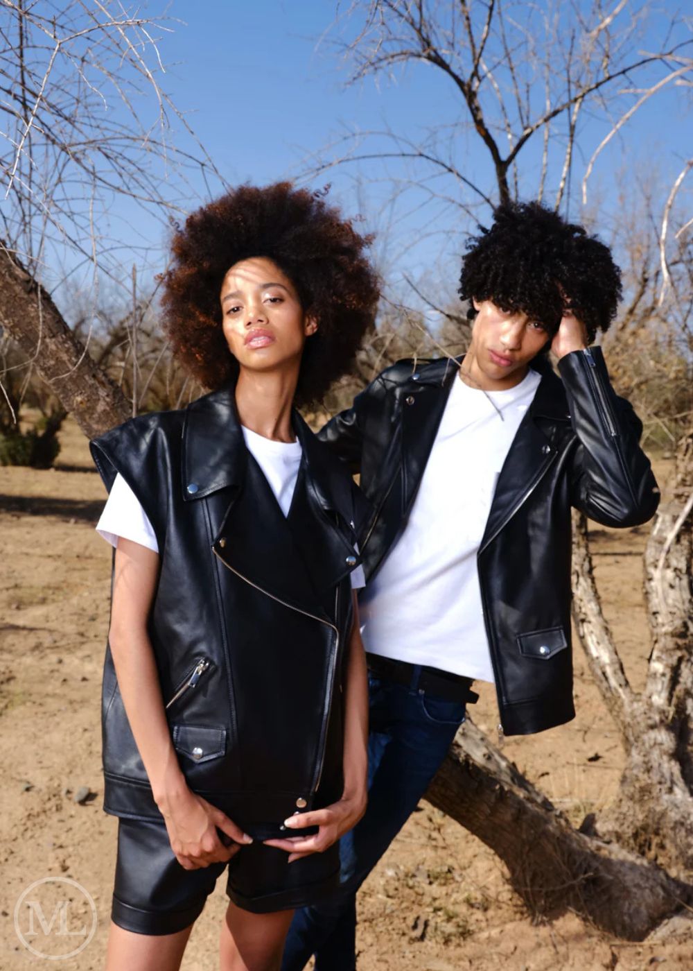 Two people wearing black leather jackets in a natural setting with trees and clear sky.