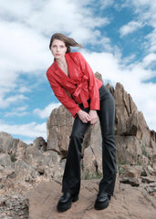 Woman wearing a red Leather Blazer jacket and black pants standing on rocky terrain with a blue sky.