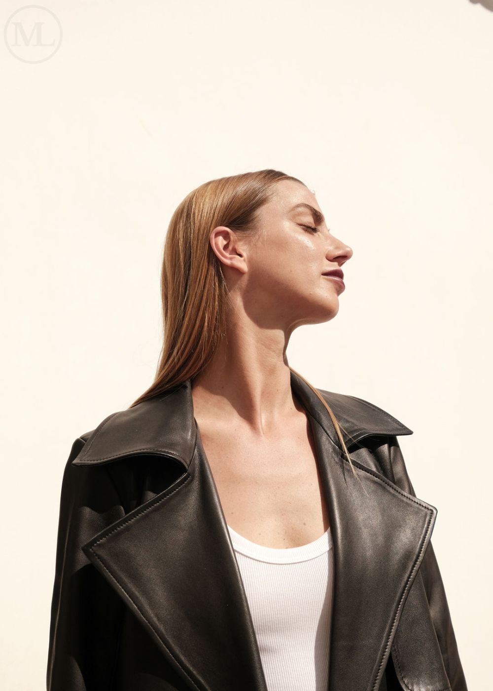 Woman wearing a black leather trench coat over a white top on a plain background