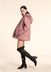 Woman wearing a fuschia leather hooded jacket and black knee-high boots on a beige background