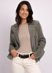 Woman wearing a gray leather jacket over a beige top and white pants on a light purple background
