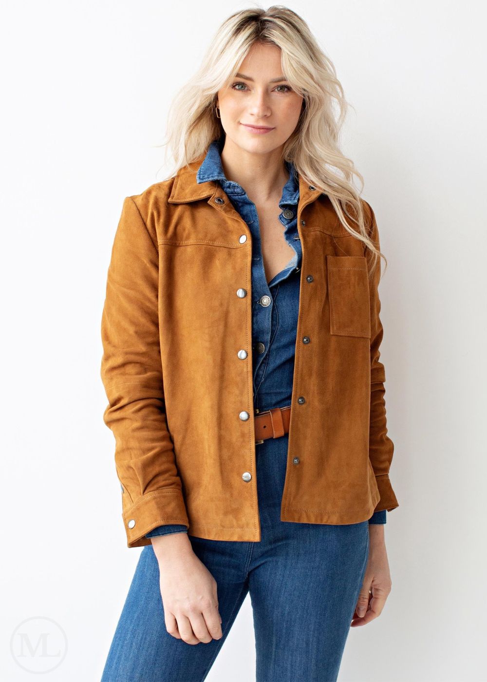 Woman wearing a cognac brown suede jacket over a denim shirt and jeans on a white background