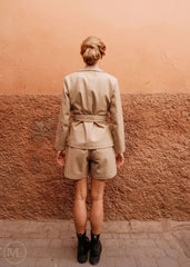 women wearing a beige leather blazer outfit standing against a textured wall.