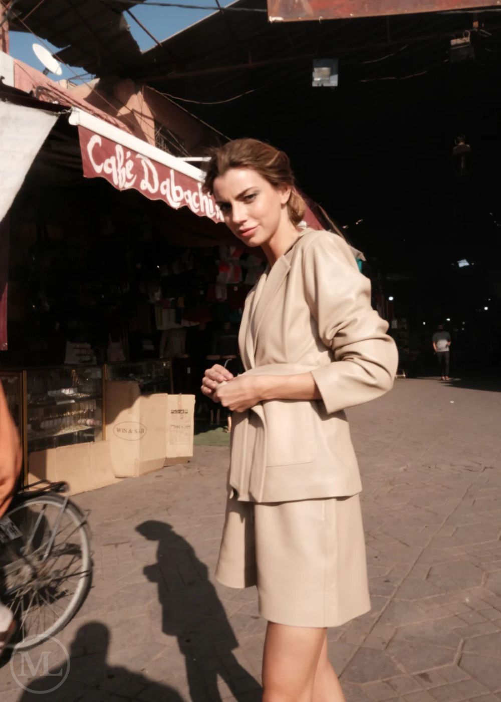 Woman in a beige leather blazer  standing on a street with a café in the background