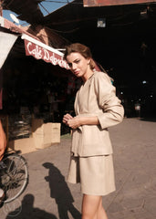 Woman in a beige leather blazer  standing on a street with a café in the background