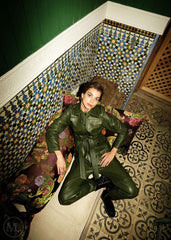 Woman wearing a olive khaki leather coat outfit sitting on a decorative bench with mosaic tiles in the background