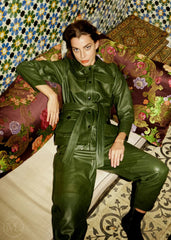 Woman wearing a olive khaki leather coat outfit sitting on a patterned couch.