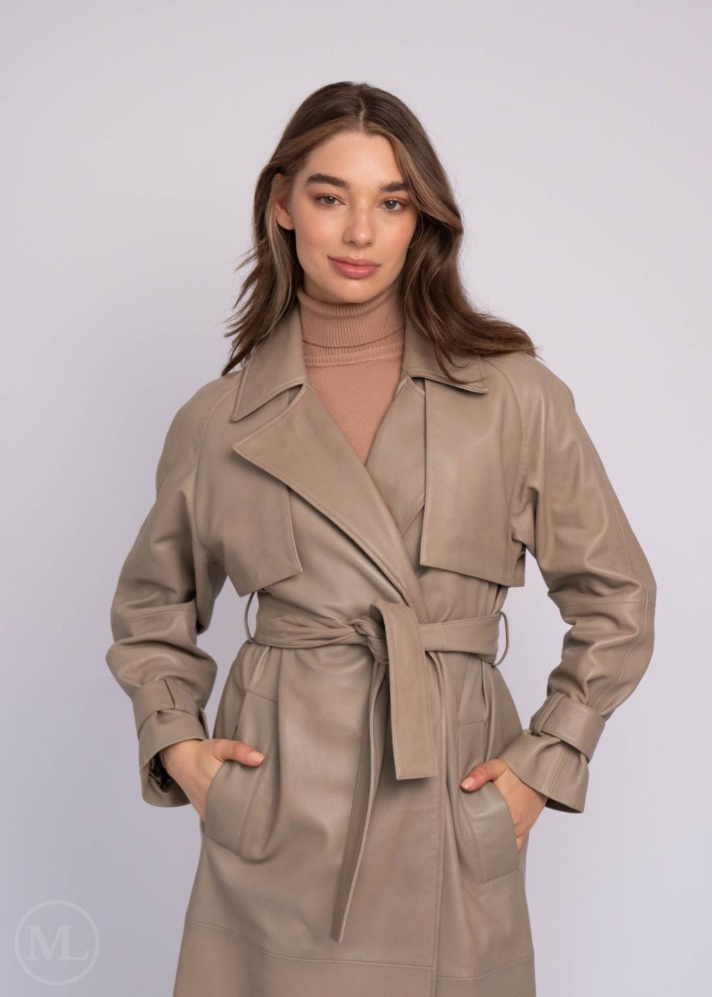 Woman wearing a taupe leather trench coat against a plain background