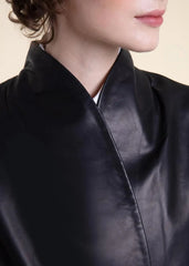 Close-up of a woman wearing a black belted wrap leather blazer coat against a beige background