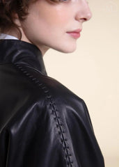 Close-up of a woman wearing a black belted wrap leather blazer coat with visible stitching on a beige background