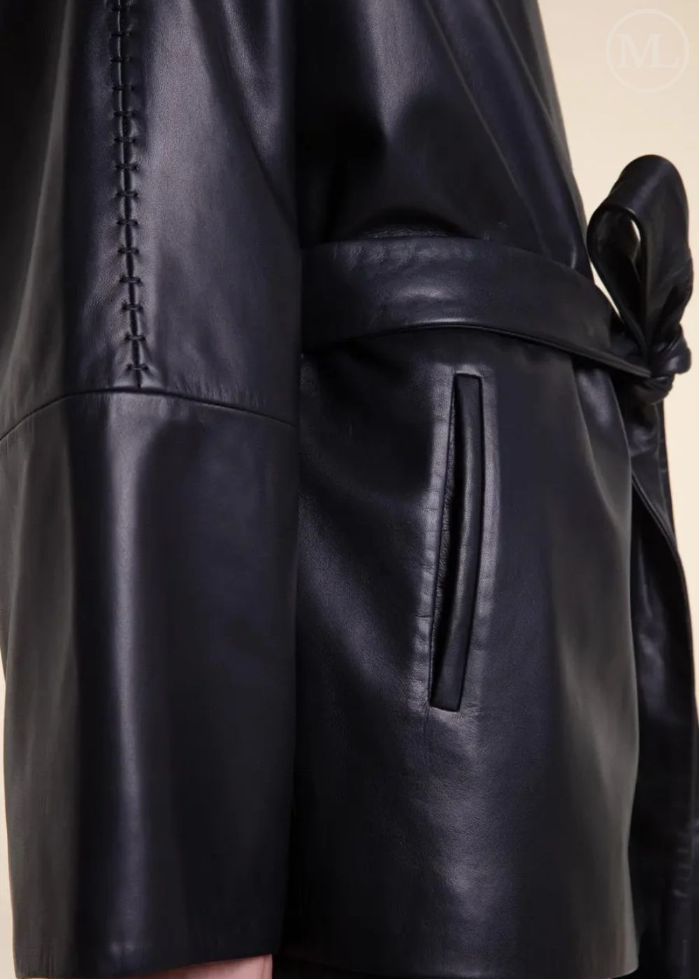 Close-up of a black belted wrap leather blazer coat on a neutral background