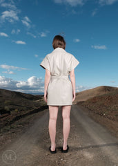 Women, ivory leather dress standing on a road with a scenic landscape and blue sky. back shot